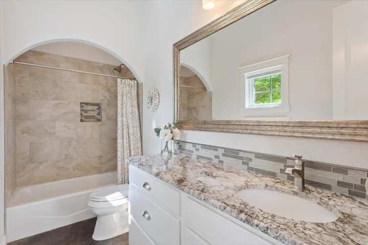 Full bathroom featuring vanity, toilet, and shower / bath combination with a large framed mirror.  Archway over the tub/shower combo...