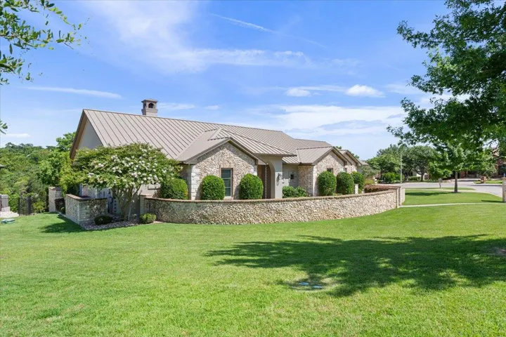 View of side of property featuring a standing seam roof, stone siding, and a lush lawn....