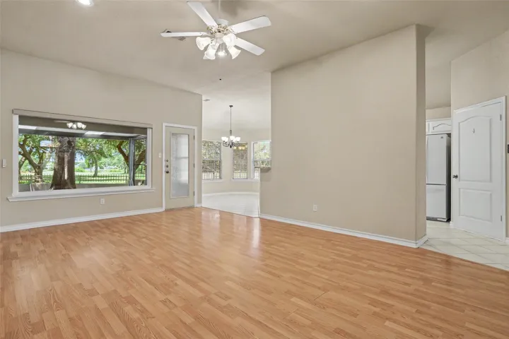 Laminate flooring extends throughout this generous living space, leading to a vibrant backyard view through wide windows.