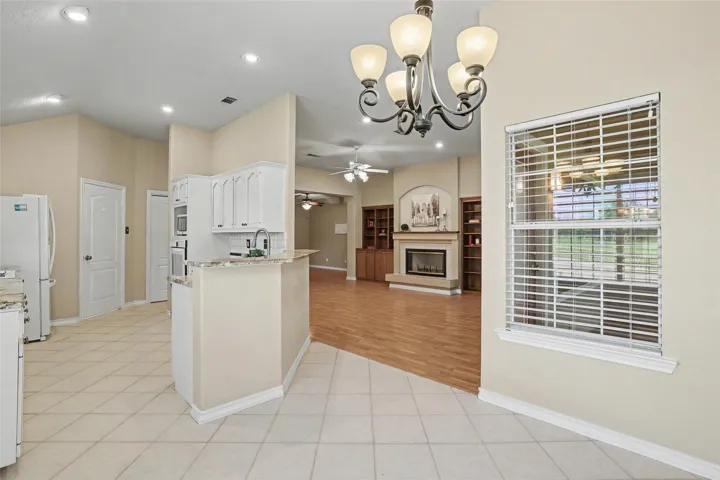 A graceful chandelier illuminates the seamless transition from kitchen to the comfortable living area with fireplace and built-in shelving.