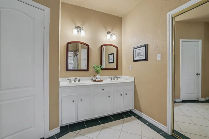 Double vanity with pristine white countertops and elegant tile flooring offers refreshing daily routines.