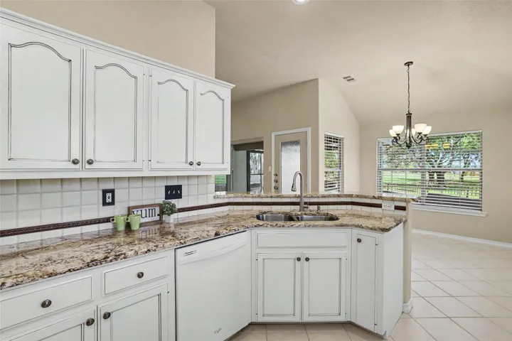 A chef's kitchen boasts granite counters, white cabinetry, a dishwasher, and a sink, flowing into an adjacent dining space with outdoor views.