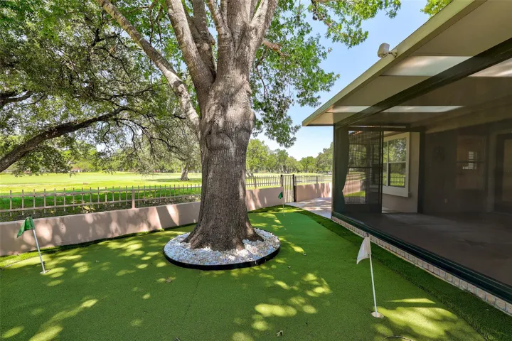 A private putting green extends from the covered patio, framed by mature trees and views of the golf course.