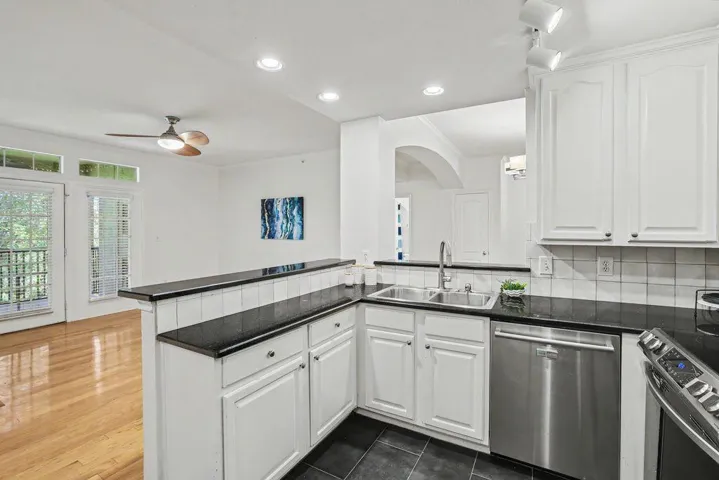 A well-equipped kitchen boasts granite counters, stainless steel appliances, and ample white cabinetry, overlooking a bright living space with balcony access.