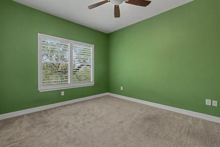 A quiet bedroom with a ceiling fan, carpet, and a sun-filled window with plantation shutters.
