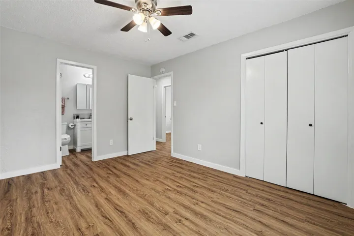 A well-lit bedroom features durable wood-look flooring and convenient access to an adjacent bathroom.