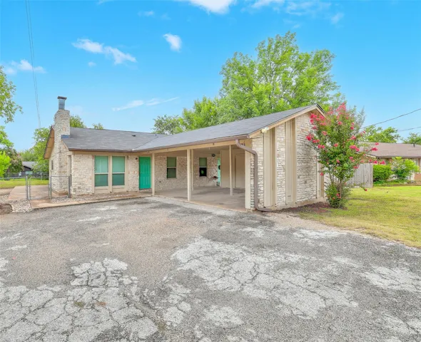 A charming stone-clad home features a covered carport and a vibrant front door.