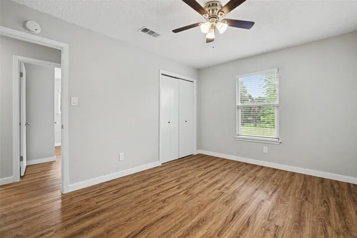 A quiet bedroom, offering wood flooring and a refreshing ceiling fan for comfortable living.