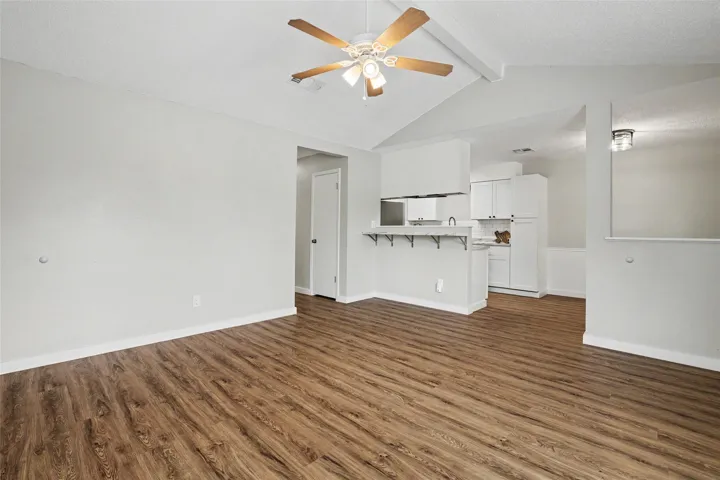 A living space offers seamless flow into the kitchen, featuring vaulted ceilings and durable wood flooring.