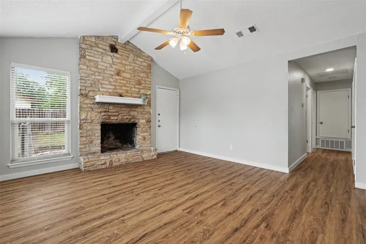 A striking stone fireplace anchors this living space, offering warmth and character beneath a vaulted ceiling with a cooling fan.
