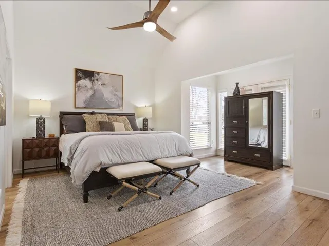 Voluminous vaulted ceilings elevate this primary bedroom, featuring light wood flooring and private outdoor access.