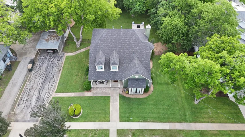 An aerial perspective reveals a charming residence nestled amidst a vibrant, tree-filled landscape.