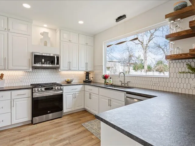 A naturally illuminated kitchen features a wide window, sleek countertops, and modern appliances.