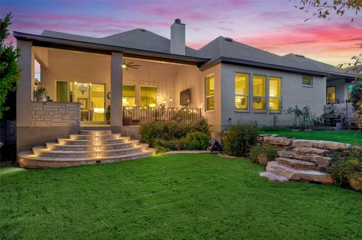 Custom stone steps lead from a covered patio to a manicured grassy lawn.