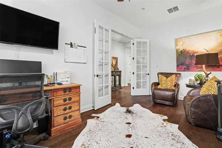 Double French doors open into this quiet workspace featuring rich hardwood flooring.