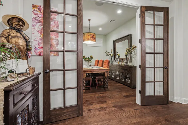 Double French doors open into an elegant dining space featuring rich hardwood flooring.