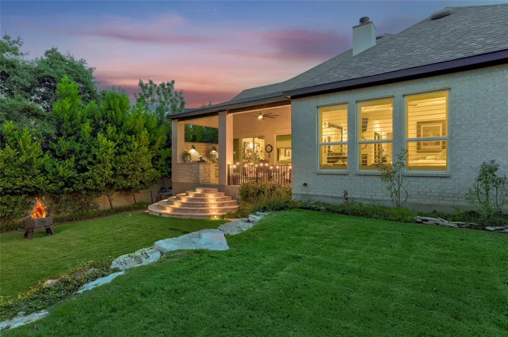 Lush green lawns lead to a covered patio and stone-lined terrace under evening skies.