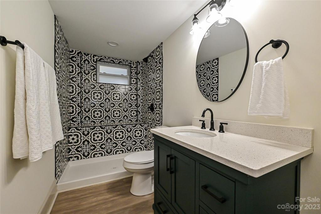 Full bath with black and white tiled shower, linen closet, and hunter green single vanity