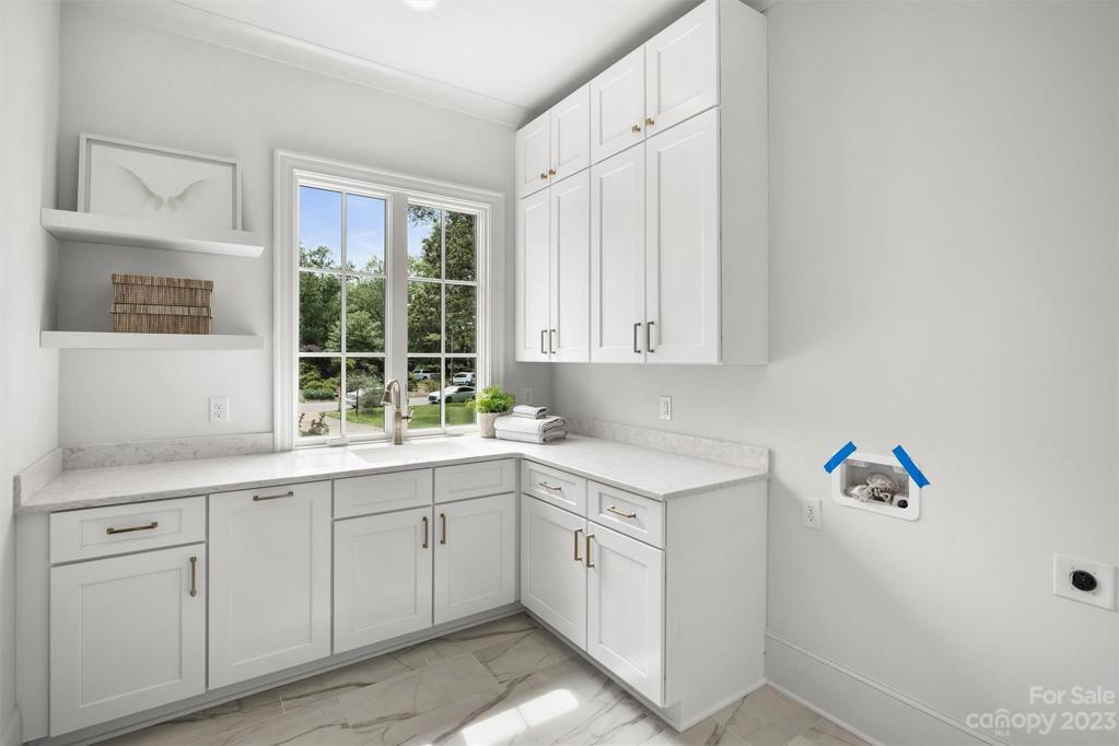 Spacious, dedicated laundry room on main floor with quartz cabinets, farmhouse sink, and additional storage closet.