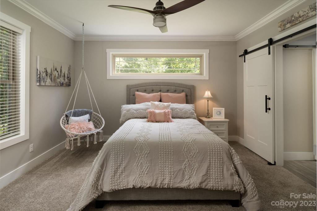 Large bedroom with barn door, pallet accent wall and adjacent full tile bathroom.