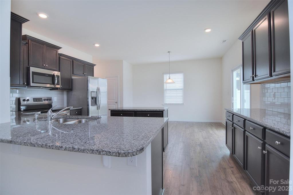 This stunning kitchen includes dark wood cabinetry, granite countertops and backsplash