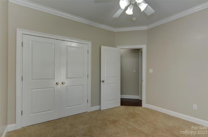 Main level bedroom 2 with ceiling fan & light, crown molding, carpet.