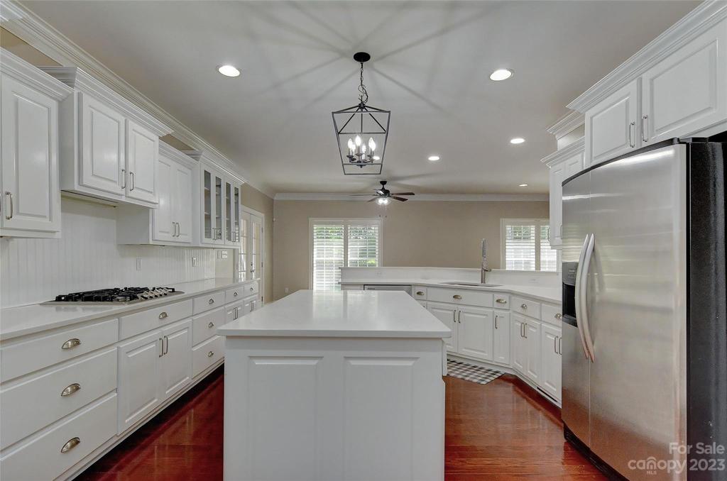 Another view showing off the lovely hardwood floors, big center island, upgraded light and the side by side refrigerator that conveys.