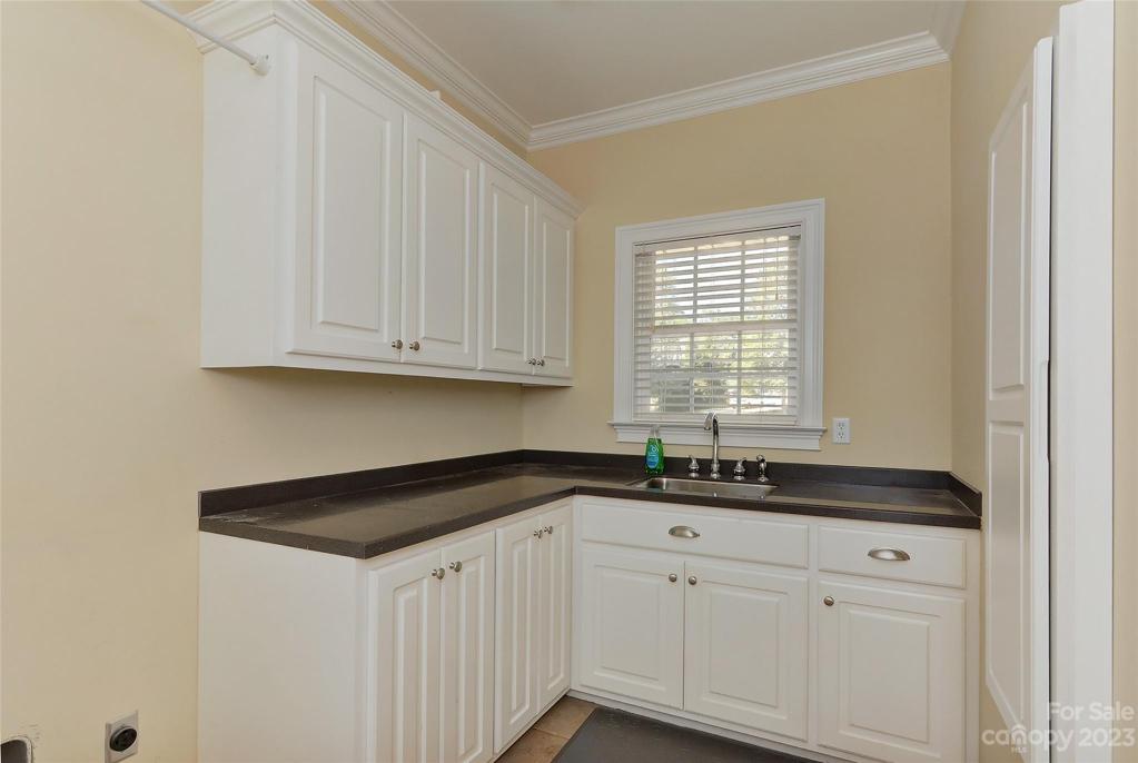 Huge mudroom/laundry room w/plenty of extra cabinetry, sink w/hand sprayer and window above, crown molding and builtin ironing board