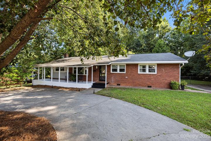 Front view of brick ranch home featuring long, low-pitch roofline and large windows along the front of the house. Of course, storm door, lively ferns and rocking chairs is a classic Southern porch look that'll never go out of style.