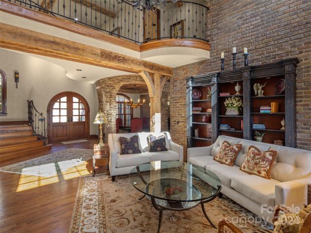 Photo looking across living room to front of the home. Notice the detail of interior brick wall, beams, custom wrought iron.And stone work/columns around dining room.