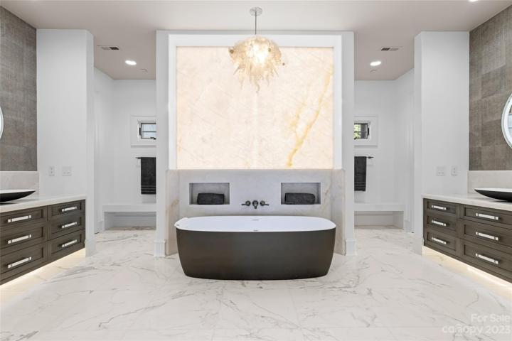 The showpiece of the owners suite is the backlit cristallo quartzite wall and custom-made hand-blown glass chandelier by Sam Stark that sets the tone of the his and hers bathroom!