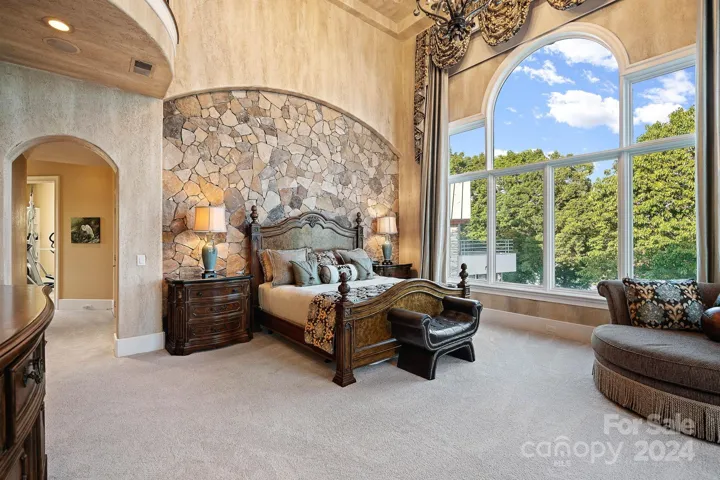 Primary bedroom with 2 story ceiling, large arched windows with electronic shades
