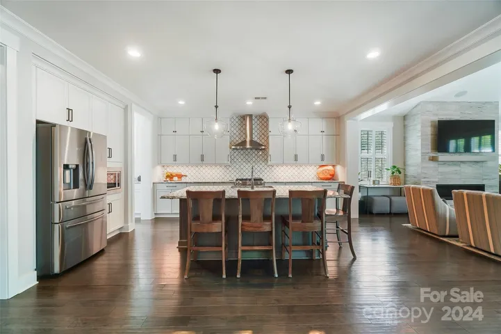 The kitchen is a chef's dream with pendant lighting, ample cabinet and granite countertop space, a custom tile backsplash, island with breakfast bar, and a convenient butler’s pantry for extra storage.