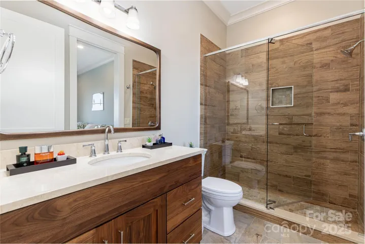 Guest suite two en-suite bath features walnut and granite vanity and wood-style shower tile.