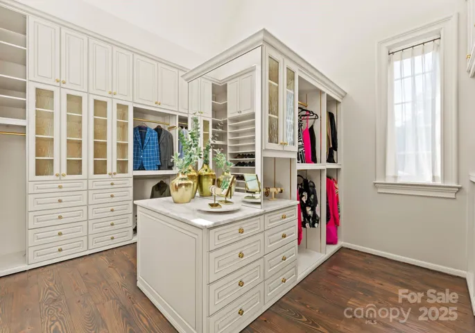 Large primary closet with built-in closet system, jewelry station, vaulted ceilings,and skylights.