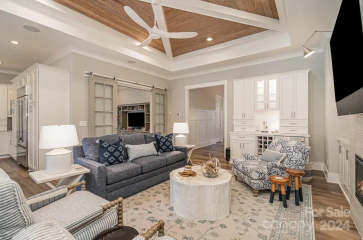 The ceiling frames the space, but also note the lovely bar area with lighted cabinets, and a beverage fridge. You can sneak a glimse of the office framed by the custom barn doors.