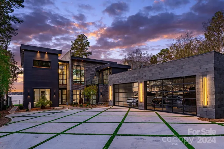 At sunset, the front elevation glows softly, showcasing the modern driveway with clean concrete slabs interspersed with linear strips of greenery, creating a sleek and contemporary aesthetic.