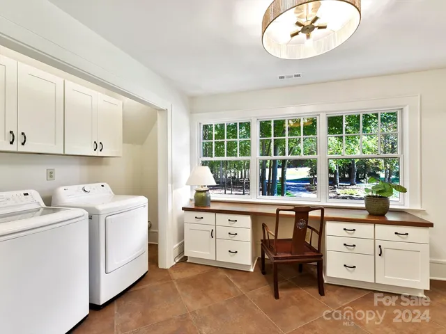 Upstairs secondary laundry room with so much space, natural lighting, desk, cabinets and hanging/folding table areas!
