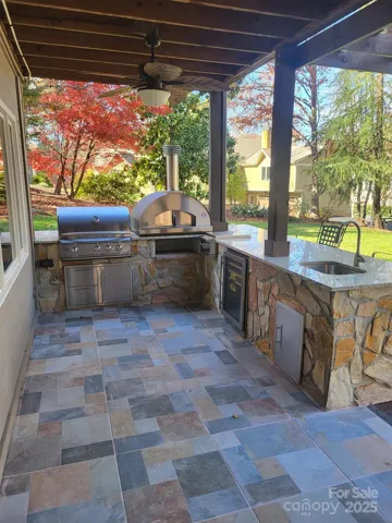 Brand new tiled patio with outdoor kitchen featuring Blaze Professional gas grill, pizza oven, stovetop burner, beverage refrigerator, and sink all surrounded by granite counters and stone-surround.