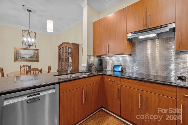 Kitchen features hardwood floors, pendant lights, recessed lights, under-cabinet lights, crown molding, tile backsplash.