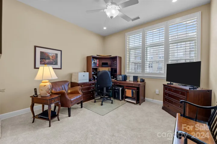 Home's second bedroom, currently used as a home office, features plantation shutters, recessed lights, ceiling fan with light, neutral carpet.