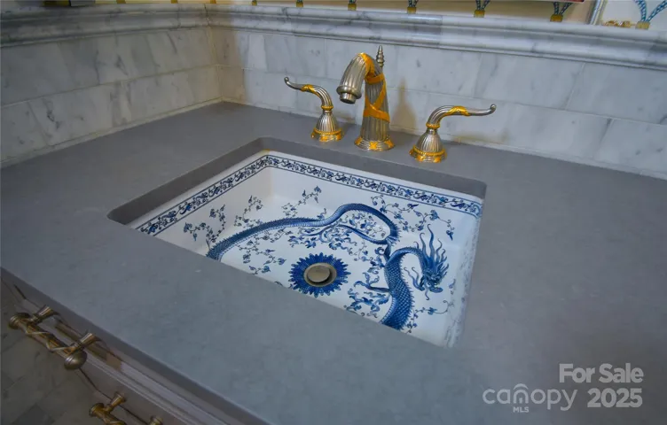 Blue and white Delft dragon motif cast iron sink adorned with gold and brushed nickel hardware, inset in gray quartz counter.
