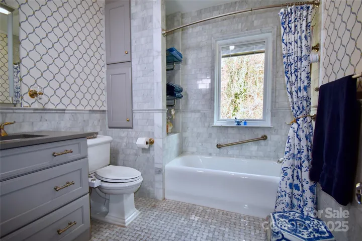 Original cast iron tub with marble mosaic tile surround and marble subway tile wainscot complement the light gray vanity with deeper gray quart top.