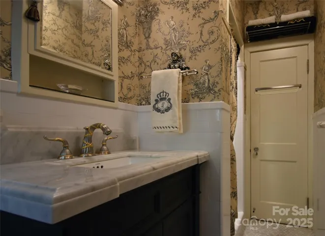 Carrera marble vanity with gold and nickel hardware, white subway tile and marble mosaic tile floor and shower are complemented by the elegant toile patterned wallpaper.