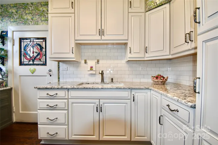 Second kitchen in unit B9, now the perfect craft room and office, features whimsical garden mortified papered walls, white subway tiled backsplash with cream colored paneled-door cabinetry and light creamy solid core countertops with contrasting veining.