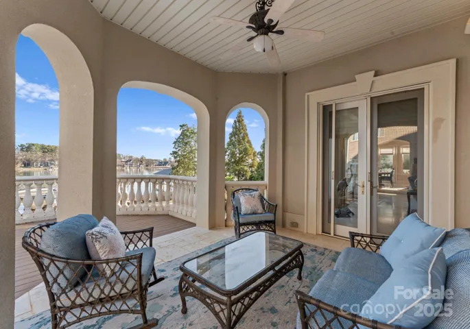 A covered sitting area with a ceiling fan, conveniently located off the great room, offering serene views of the pool area and lake beyond.