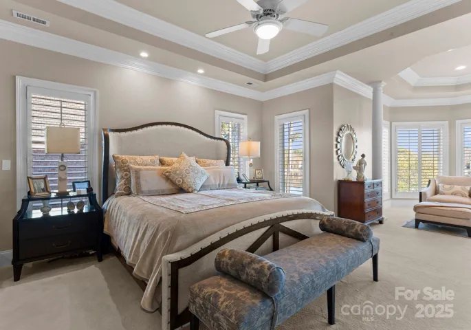 Spacious primary suite featuring tray ceilings, crown molding, and a cozy sitting area. The suite also includes a fireplace, two walk-in closets, and a grand ensuite, offering ample space and luxury for relaxation and convenience.