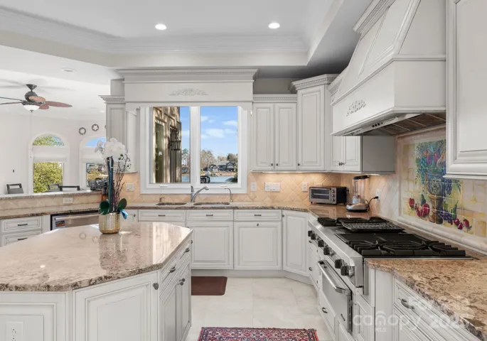 A kitchen window offers serene lake views, while the Wolf cooktop, double oven, refrigerator, and microwave ensure top-tier functionality. Stone countertops complement the artistic travertine backsplash, adding a sophisticated touch to this culinary haven.