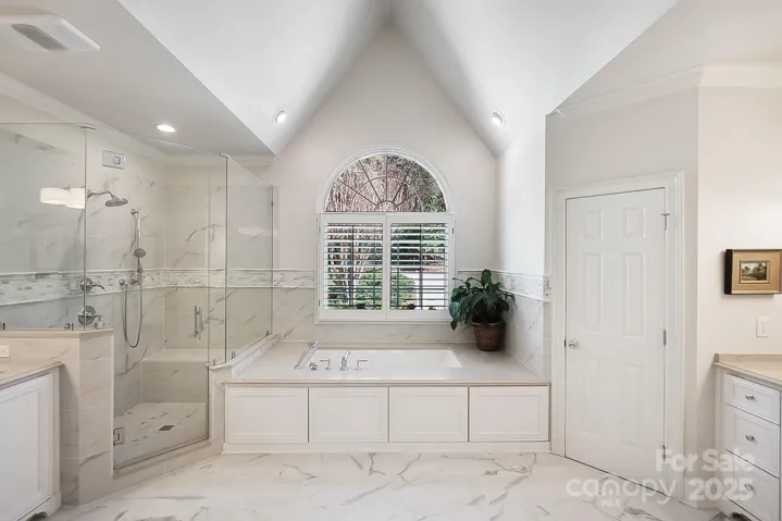 Vaulted primary bath with dual vanities, jetted tub, and large walk-in shower