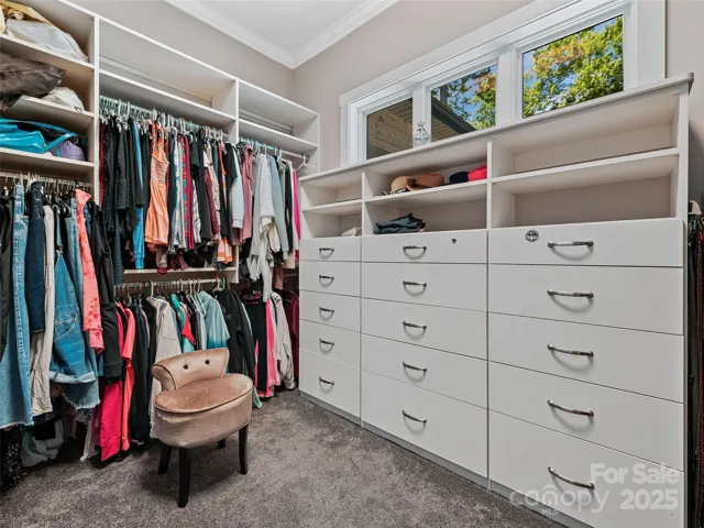 Spacious walk-in closet with crown moulding and custom built-in with drawers and adjustable shelving